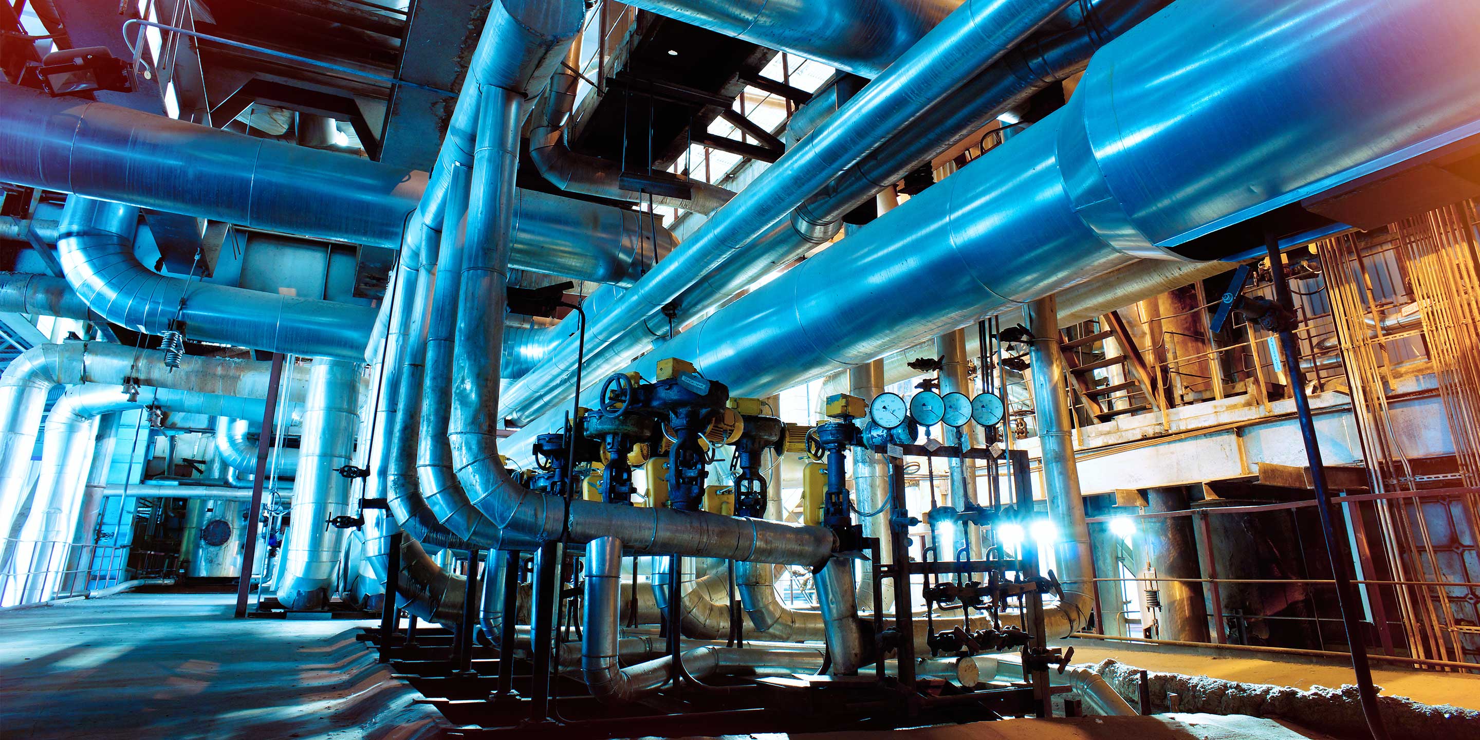 A complex network of large blue pipes, gauges, and valves in a well-lit industrial environment. Ideal for illustrating fluid or gas processing systems, engineering infrastructure, or industrial automation.